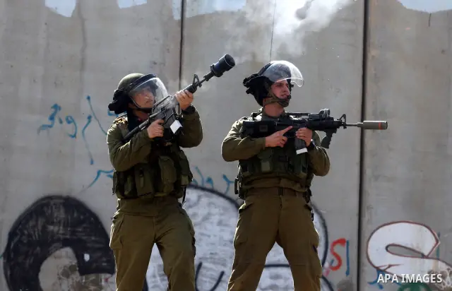 Israeli soldiers standing before the separation wall, protect themselves against teargas during a protest next to the checkpoint of Kalandia, West Bank, 08 March 2012, North of Jerusalem, during a rally to mark the Inter...