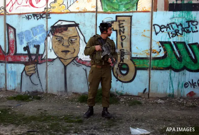 Israeli soldiers standing before the separation wall, protect themselves against teargas during a protest next to the checkpoint of Kalandia, West Bank, 08 March 2012, North of Jerusalem, during a rally to mark the Inter...