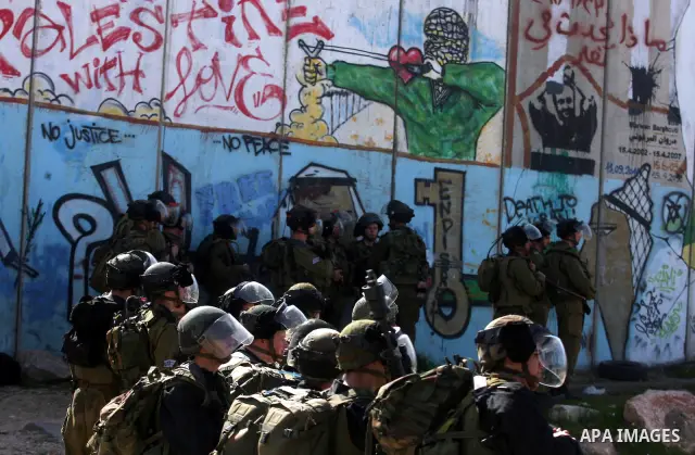 Israeli soldiers standing before the separation wall, protect themselves against teargas during a protest next to the checkpoint of Kalandia, West Bank, 08 March 2012, North of Jerusalem, during a rally to mark the Inter...