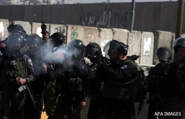 Israeli soldiers standing before the separation wall, protect themselves against teargas during a protest next to the checkpoint of Kalandia, West Bank, 08 March 2012, North of Jerusalem, during a rally to mark the Inter...