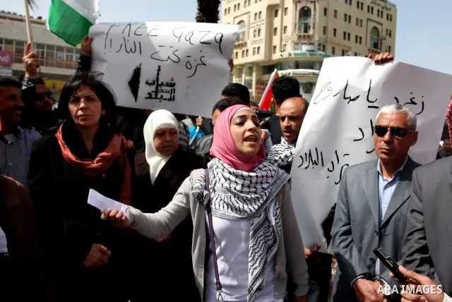 A Palestinian woman shouts slogans during a rally in support of Palestinians in Gaza Strip in the West Bank city of Ramallah, Sunday, March. 11, 2012. The Arabic text on the banner reads: g "Free Gaza, Gaza under fire"....