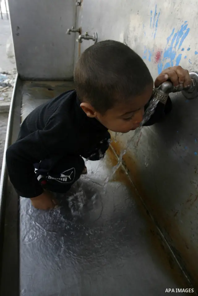 Palestinian children filling plastic bottles and jerry cans with drinking water from a public tap at the United Nations Relief and Works Agency (UNRWA) headquarters in the southern Gaza Strip refugee camp of Rafah on Mar...