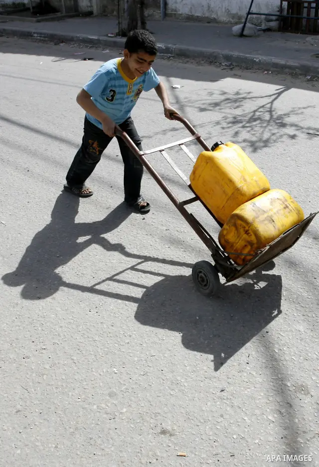 Palestinian children filling plastic bottles and jerry cans with drinking water from a public tap at the United Nations Relief and Works Agency (UNRWA) headquarters in the southern Gaza Strip refugee camp of Rafah on Mar...