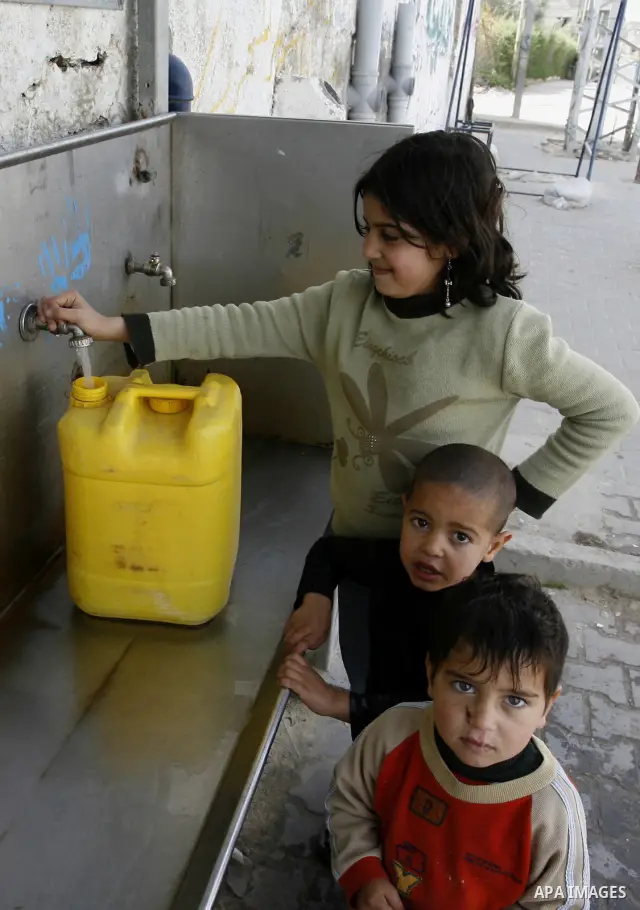 Palestinian children filling plastic bottles and jerry cans with drinking water from a public tap at the United Nations Relief and Works Agency (UNRWA) headquarters in the southern Gaza Strip refugee camp of Rafah on Mar...