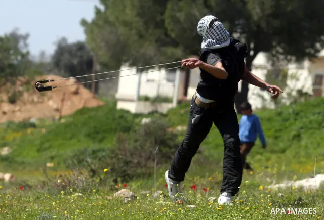 A Palestinian protester swings a sling at Israeli troops during a protest against the expansion of the nearby Jewish settlement of Halamish in the West Bank village of Nabi Saleh, near Ramallah, Friday, March 23, 2012. P...