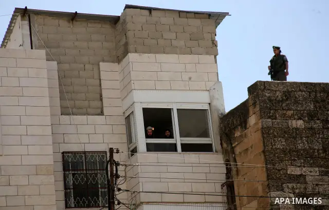 An Israeli settler looks out the window of an occupied Palestinian house as an Israeli soldier stands guard in the centre of Hebron in the occupied West Bank on March 29, 2012. Dozens of Jewish settlers took over the Pal...