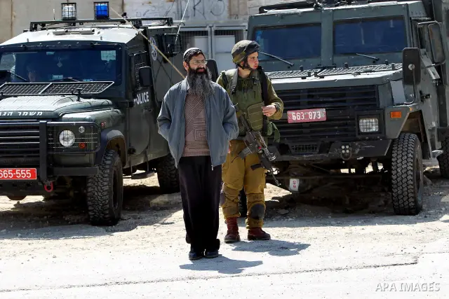 Israeli settlers walk past Israeli border policemen standing guard outside an occupied Palestinian house after dozens of Jewish settlers took over the property overnight, claiming they have legal ownership, in the occupi...
