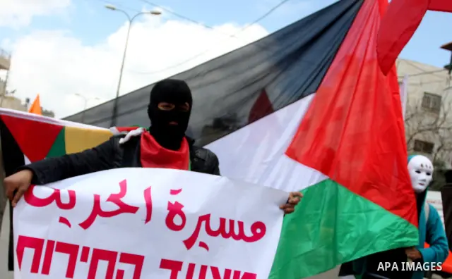 A masked Palestinian protester holds his national flag as he commemorates Land Day in Qalandia which lies between Jerusalem and the West Bank city of Ramallah on March 30, 2012. Land Day marks the annual event that comme...