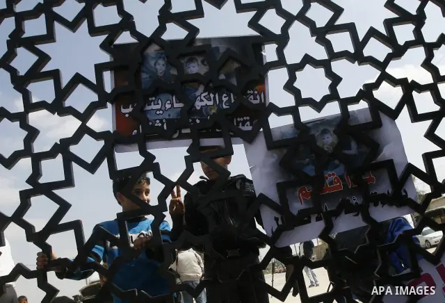 Palestinian boys hold a poster of three children who were killed in a fire caused by a candle being used due to lack of electricity during a protest against the electricity crisis near the southern Gaza Strip's Rafah bor...