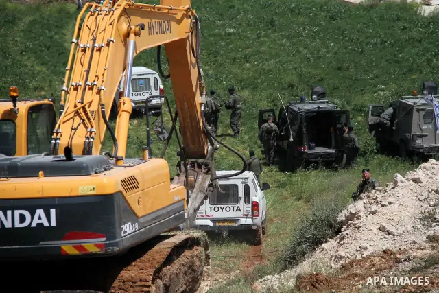 Israeli Border Police stand by as a security bulldozer demolishes a water storage tank owned by the Palestinians in the village of Dura, outside the West Bank city of Hebron, 16 April 2012. The reservoir building was dem...