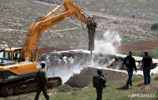 Israeli Border Police stand by as a security bulldozer demolishes a water storage tank owned by the Palestinians in the village of Dura, outside the West Bank city of Hebron, 16 April 2012. The reservoir building was dem...