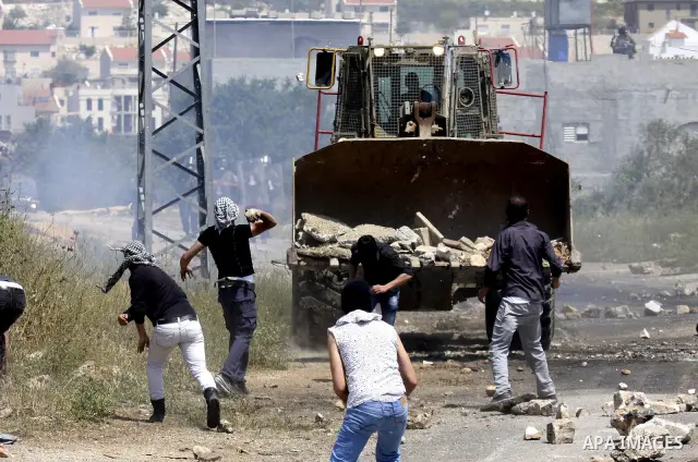 Palestinian protesters throws a stones at an Israeli military digger as it removes a barricade during a demonstration against the expropriation of Palestinian land by Israel in the village of Kafr Qaddum, near the northe...