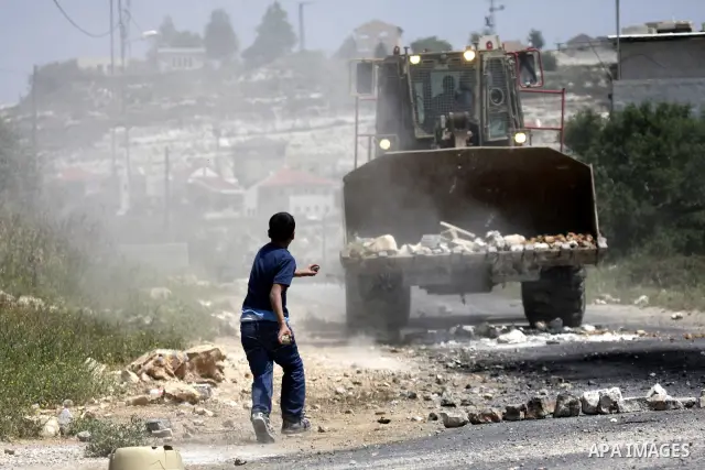 Palestinian protesters throws a stones at an Israeli military digger as it removes a barricade during a demonstration against the expropriation of Palestinian land by Israel in the village of Kafr Qaddum, near the northe...