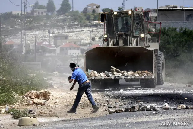 Palestinian protesters throws a stones at an Israeli military digger as it removes a barricade during a demonstration against the expropriation of Palestinian land by Israel in the village of Kafr Qaddum, near the northe...