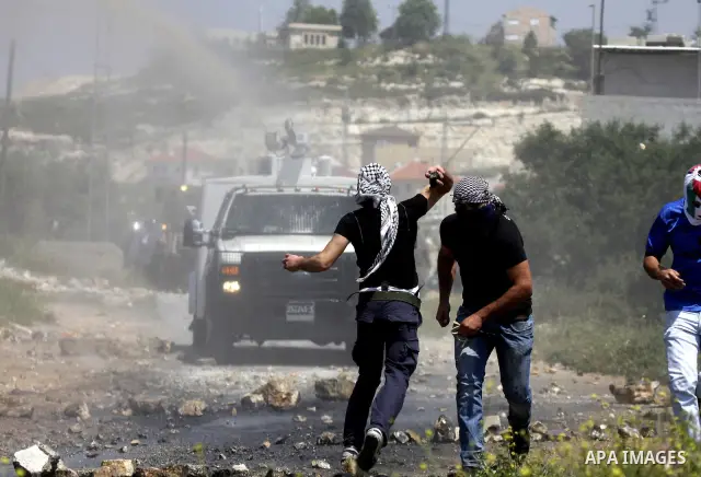 Palestinian protesters throws a stones at an Israeli military digger as it removes a barricade during a demonstration against the expropriation of Palestinian land by Israel in the village of Kafr Qaddum, near the northe...