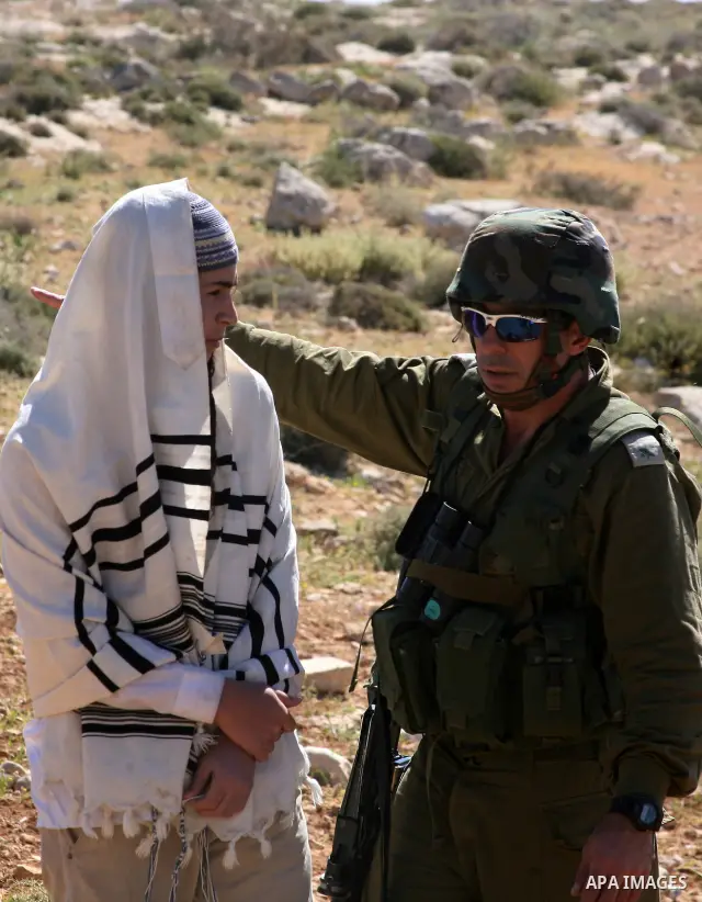Israeli Jewish settlers look on as Israeli soldiers move Palestinian farmers and shepherds off their land to allow the settlers to farm the land near the Maaon Jewish settlement, just south of the Palestinian village of...