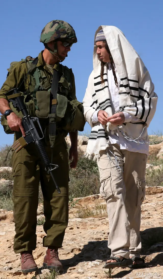 Israeli Jewish settlers look on as Israeli soldiers move Palestinian farmers and shepherds off their land to allow the settlers to farm the land near the Maaon Jewish settlement, just south of the Palestinian village of...