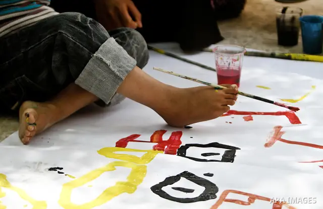 A Palestinian disabled child uses his feet to draw and paint pictures at a charity association during a celebration in Gaza city on April 23,2012. Photo by Ali Jadallah