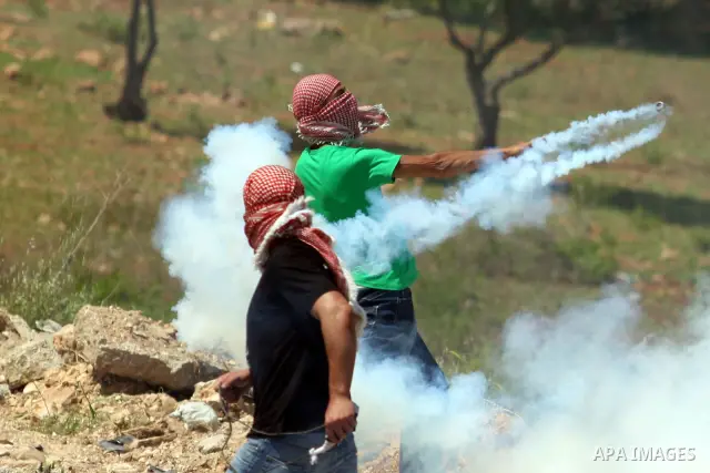 A Palestinian demonstrator returns a tear gas canister towards Israeli soldiers during clashes with Israeli soldiers at the Bitwonia crossing outside the Israeli military prison of Ofer, on Israel's 64th Independence Day...