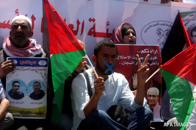 Palestinian protesters hold pictures of Palestinian prisoners held in Israel, as he faces Israeli soldiers at the Bitwonia crossing outside the Israeli military prison of Ofer, on Israel's 64th Independence Day, 26 April...