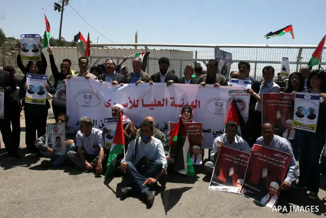 Palestinian protesters hold pictures of Palestinian prisoners held in Israel, as he faces Israeli soldiers at the Bitwonia crossing outside the Israeli military prison of Ofer, on Israel's 64th Independence Day, 26 April...