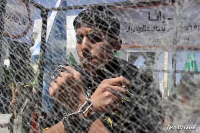A Palestinian youth sits in side a mock cage with his hands tied in chains during a protest after Friday prayer to call for the release of Palestinian prisoners held in Israeli jails in Gaza City on April 27, 2012. Some...