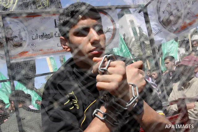 A Palestinian youth sits in side a mock cage with his hands tied in chains during a protest after Friday prayer to call for the release of Palestinian prisoners held in Israeli jails in Gaza City on April 27, 2012. Some...