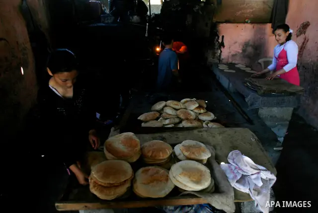 Palestinian girls help baker to bake loaves of bread in a traditional mud oven in Rafah refugee camp, southern Gaza Strip on April 28, 2012. Photo by Eyad Al Baba