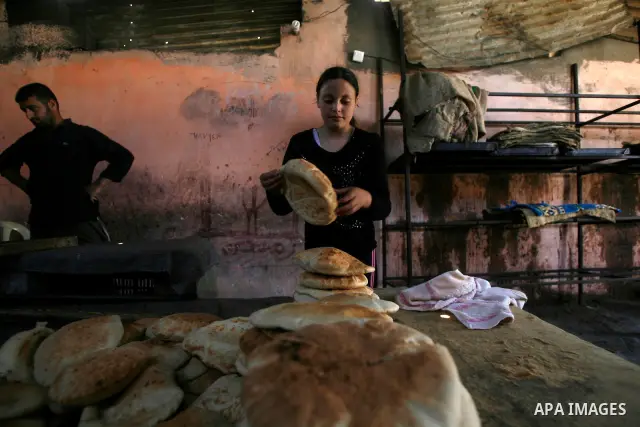 A Palestinian girl helps baker to bake loaves of bread in a traditional mud oven in Rafah refugee camp, southern Gaza Strip on April 28, 2012. Photo by Eyad Al Baba