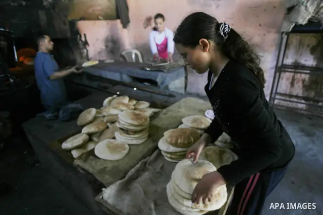 Palestinian girls help baker to bake loaves of bread in a traditional mud oven in Rafah refugee camp, southern Gaza Strip on April 28, 2012. Photo by Eyad Al Baba