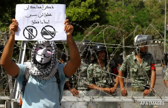An Egyptian protester wearing a Guy Fawkes mask holds a sign reading "Remind your enemies that we will never forget what they have done" during a demonstartion against the interim military leadership outside the defence...