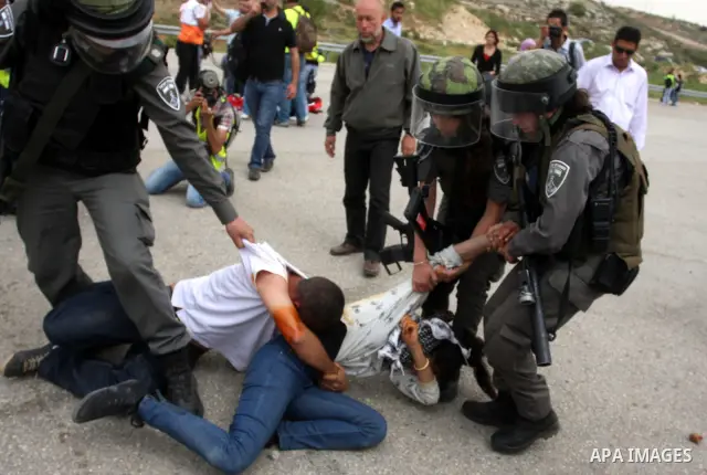 Palestinian protesters who were hit with pepper spray by Israeli border police, lie on the ground as they try to prevent Israeli troops from detaining one of them, during clashes outside Ofer prison near the West Bank ci...