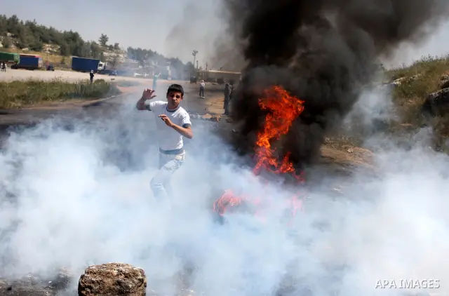 A Palestinian youth kicks a flaming tire during clashes with Israeli soldiers outside the Ofer Prison close to the West Bank city of Ramallah, following a march in support of Palestinian prisoners of on hunger strike whi...