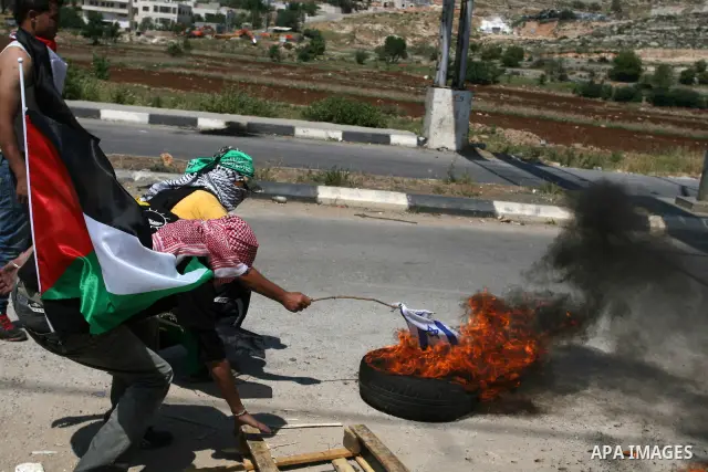 A Palestinian protesters burn a tire and Israeli flag during clashes outside the Ofer Prison close to the West Bank city of Ramallah, following a demonstration in support of Palestinian prisoners on hunger strike in Isra...