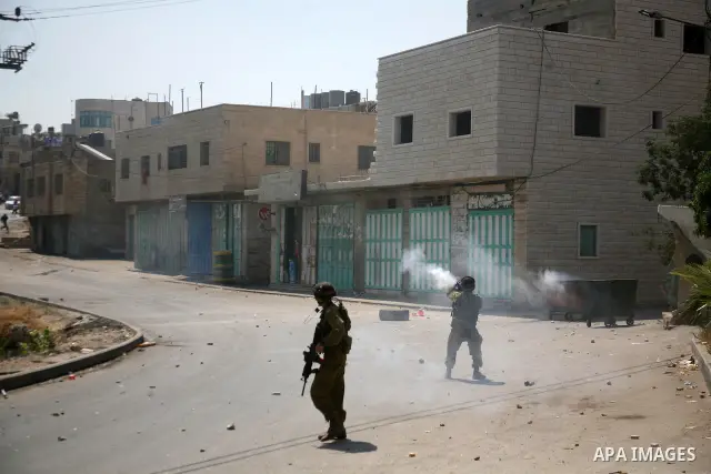Palestinian protesters run for cover from the teargas fired by Israeli soldiers during clashes broke out in the village of Beit Ommar, near the northern West Bank city of Hebron, following a demonstration solidarity with...