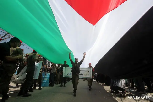 Palestinian Hamas security walk under a large Palestinian flag during a rally marking Al-Nakba, commemorating the displacement of Palestinians in 1948 due to the declaration of the state of Israel, in Gaza City, Gaza Str...