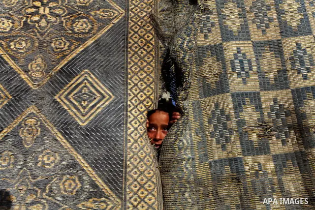 A Palestinian child peers through hanging floor matting at her home in the Shati Palestinian refugee camp in Gaza City on May 15, 2012, as Palestinians and Arab-Israelis marked Nakba day, which commemorates the exodus of...