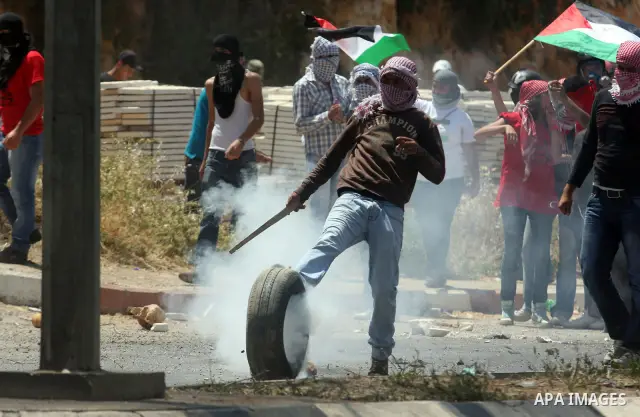 A masked Palestinian kicks a burning tire towards Israeli troops, during clashes on Nakba Day near Ofer prison, near Ramallah, the West Bank, 15 May 2012. Thousands marched in the West Bank and Gaza Strip, commemorating...