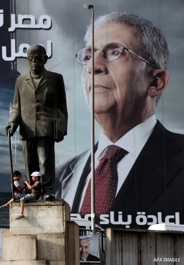 Egyptian boys sit underneath a statue of Egyptian novelist Naguib Mahfouz seen in front of a huge election campaign banner for former foreign minister and Arab League chief and presidential candidate, Amr Mussa, in Cairo...