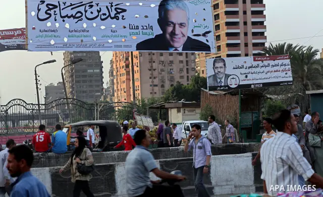 Egyptians walk behind an election campaign banner for the presidential candidate, Hamdin Sabahi, in Cairo on May 21, 2012. The Supreme Council of the Armed Forces urged Egyptians to accept the results of a looming presid...
