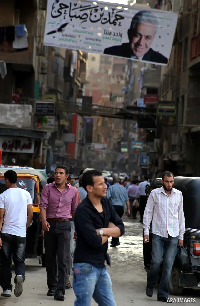 Egyptians walk behind an election campaign banner for the presidential candidate, Hamdin Sabahi, in Cairo on May 21, 2012. The Supreme Council of the Armed Forces urged Egyptians to accept the results of a looming presid...