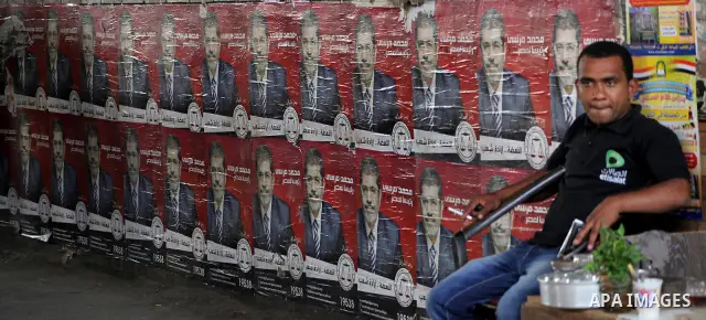 An Egyptian man sits in front of election campaign posters for the Muslim Brotherhood's presidential candidate, Mohammed Mursi, in Cairo on May 21, 2012. The Supreme Council of the Armed Forces urged Egyptians to accept...