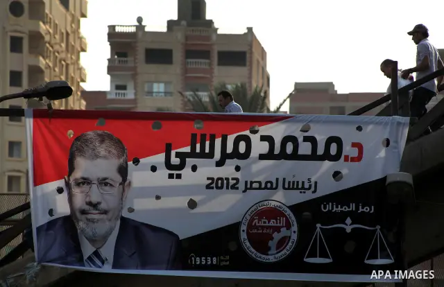 Egyptians walk behind an election campaign banner for the Muslim Brotherhood's presidential candidate, Mohammed Mursi, in Cairo on May 21, 2012. The Supreme Council of the Armed Forces urged Egyptians to accept the resul...