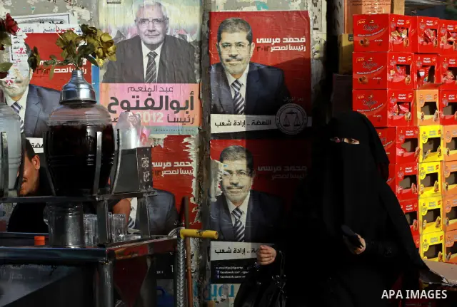 An Egyptian woman buys a drink in front of election campaign posters for the Muslim Brotherhood's presidential candidate, Mohammed Mursi, in Cairo on May 21, 2012. The Supreme Council of the Armed Forces urged Egyptians...