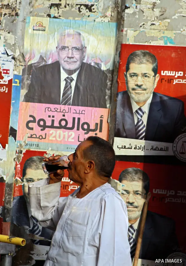 An Egyptian man drinks in front of election campaign posters for the Muslim Brotherhood's presidential candidate, Mohammed Mursi, in Cairo on May 21, 2012. The Supreme Council of the Armed Forces urged Egyptians to accep...