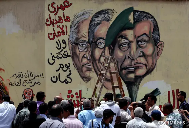 An artist writes a slogan in Arabic that reads "I will never give you peace" next to a graffiti picturing the morphed faces of ousted president Hosni Mubarak (R) and military ruler Hussein Tantawi and presidential candid...