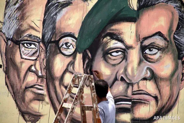 An artist writes a slogan in Arabic that reads "I will never give you peace" next to a graffiti picturing the morphed faces of ousted president Hosni Mubarak (R) and military ruler Hussein Tantawi and presidential candid...