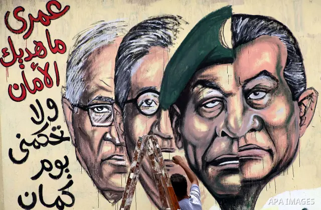 An artist writes a slogan in Arabic that reads "I will never give you peace" next to a graffiti picturing the morphed faces of ousted president Hosni Mubarak (R) and military ruler Hussein Tantawi and presidential candid...