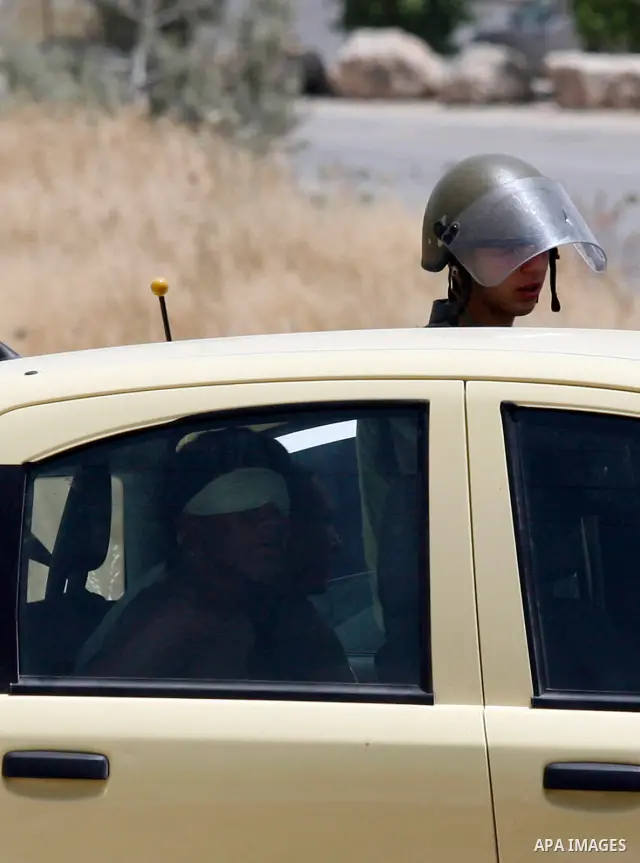 An Israeli soldier looks at a blindfolded and handcuffed Palestinian youth, as he sits in the back of a car after he was arrested at the Hawara checkpoint on the southern edge of the northern Palestinian city of Nablus i...