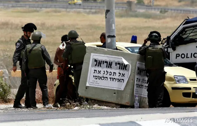 Israeli soldiers look at a blindfolded and handcuffed Palestinian youth, as he sits in the back of a car after he was arrested at the Hawara checkpoint on the southern edge of the northern Palestinian city of Nablus in t...